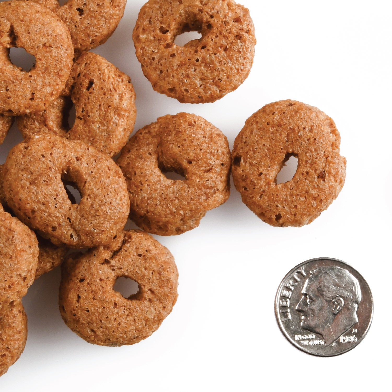 Brown dog treats with a coin for scale on a white background